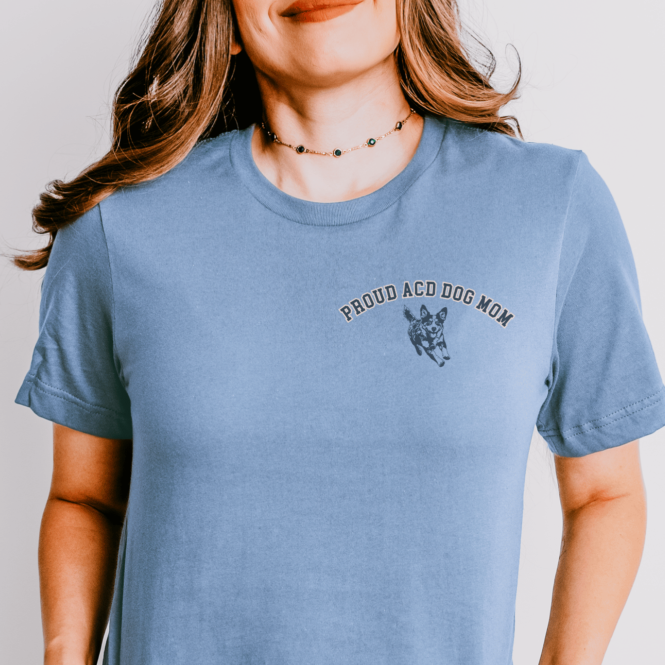 Person wearing a blue t-shirt with 'Proud ACDog Mom' text and dog graphic on a plain background