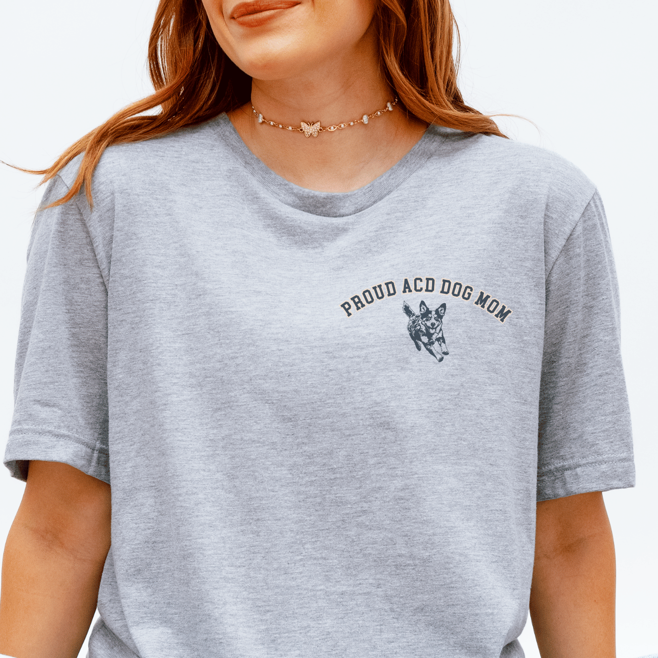 Person wearing a gray t-shirt with 'Proud ACDog Mom' text and graphic, sitting on a yellow and white striped rug.