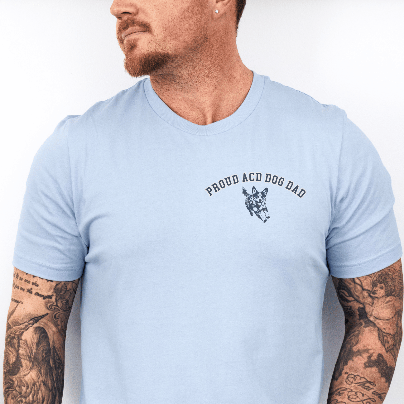 Man wearing a light blue t-shirt with text and graphics, standing against a white wall.